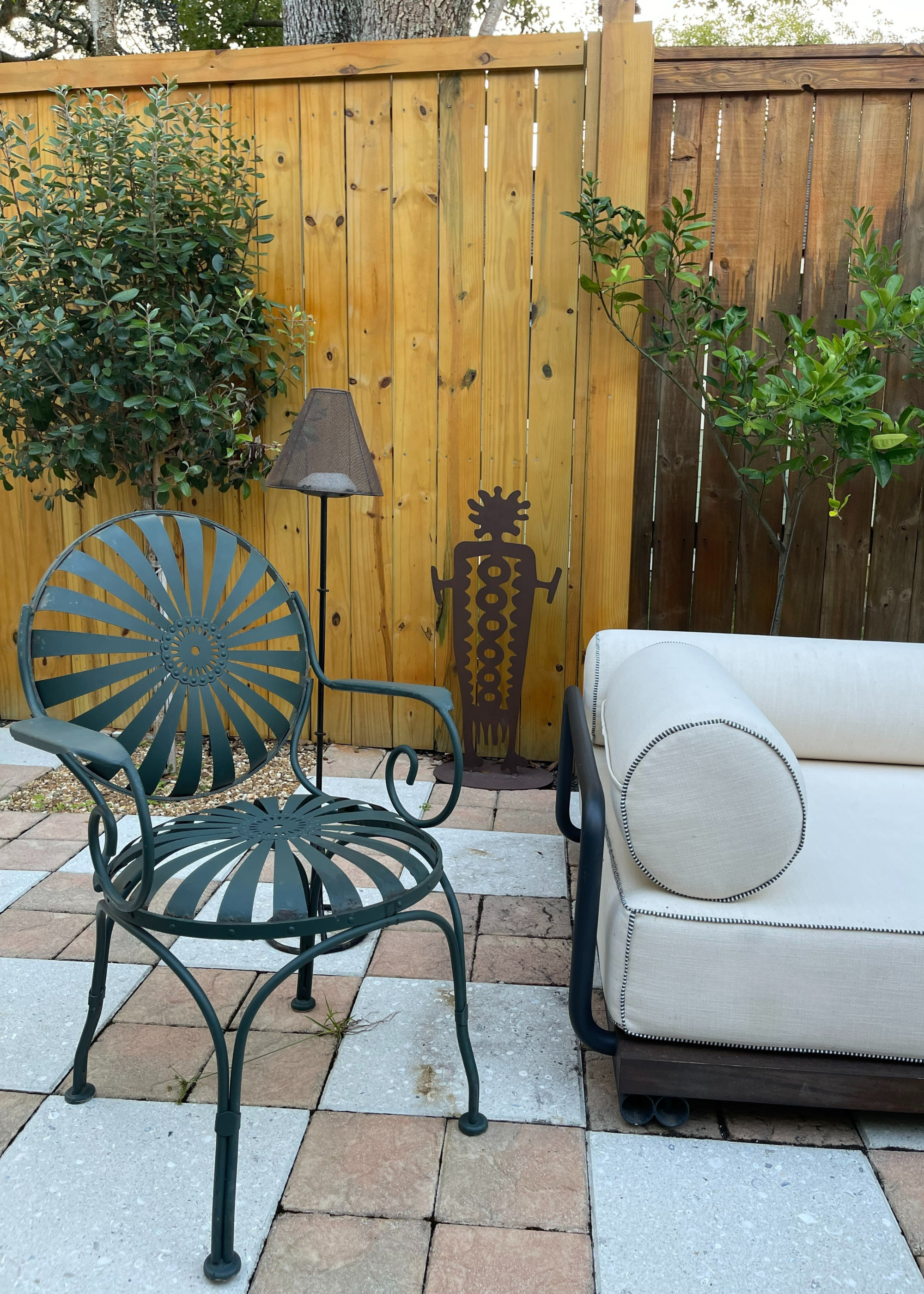 An outdoor bistro chair beside a floor lamp, an iron sculpture and a sofa