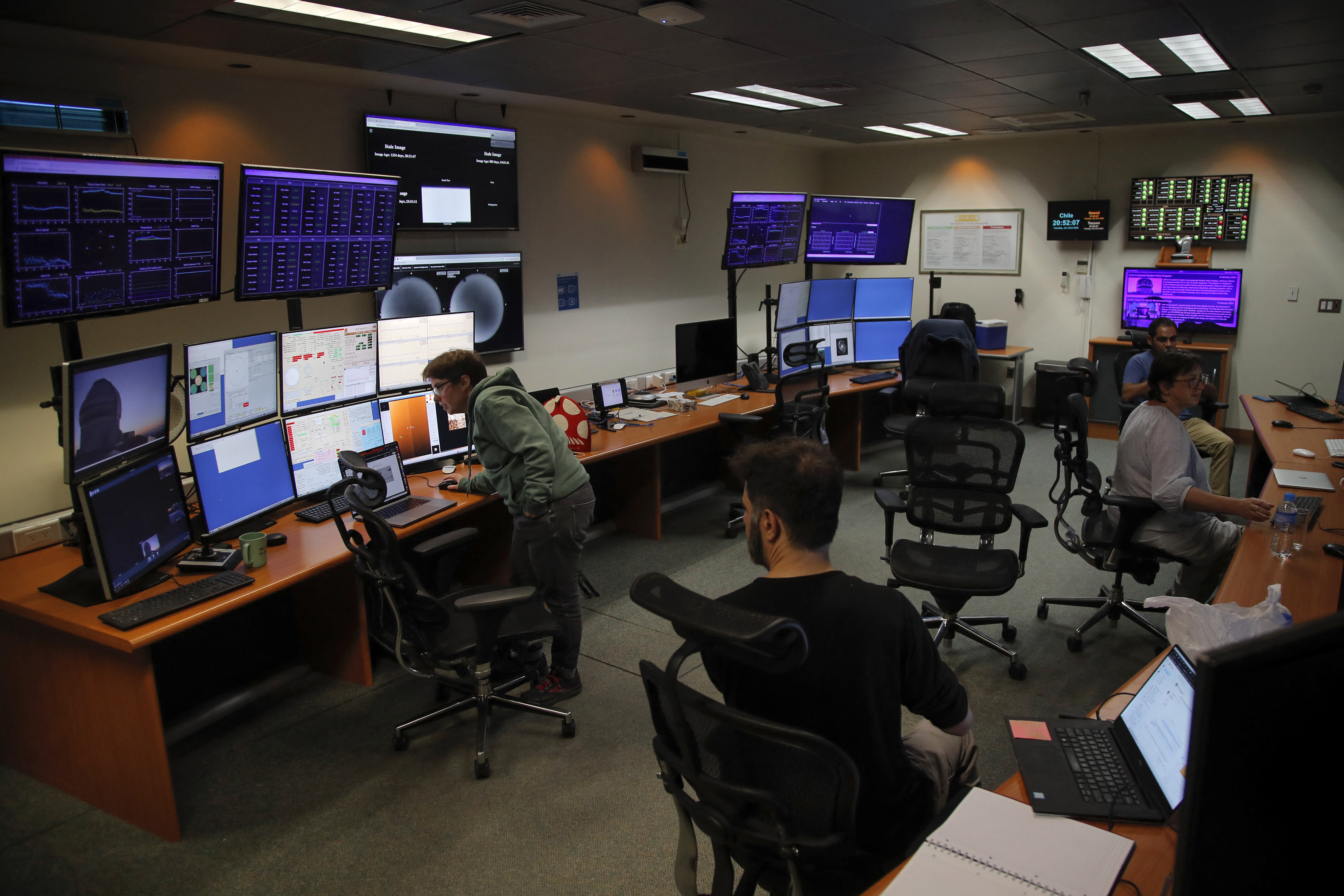 A group of people sitting in front of desks and computer monitors