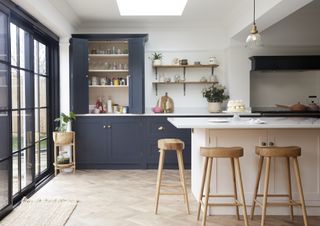blue and white kitchen with enclosed cabinet, open shelving, island, white countertops, herringbone floor, wooden stools