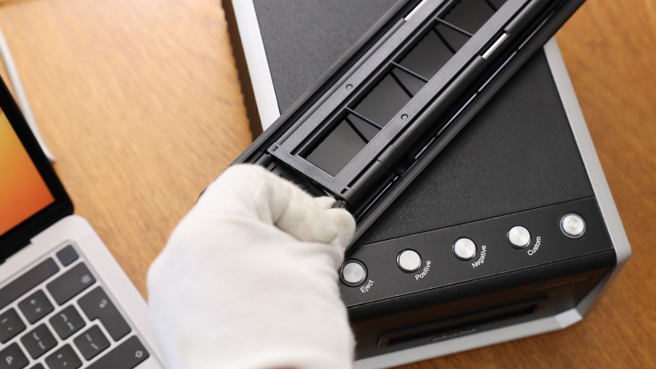 A hand in a white glove putting a strip of film into a film holder for the Plustek OpticFilm 135i