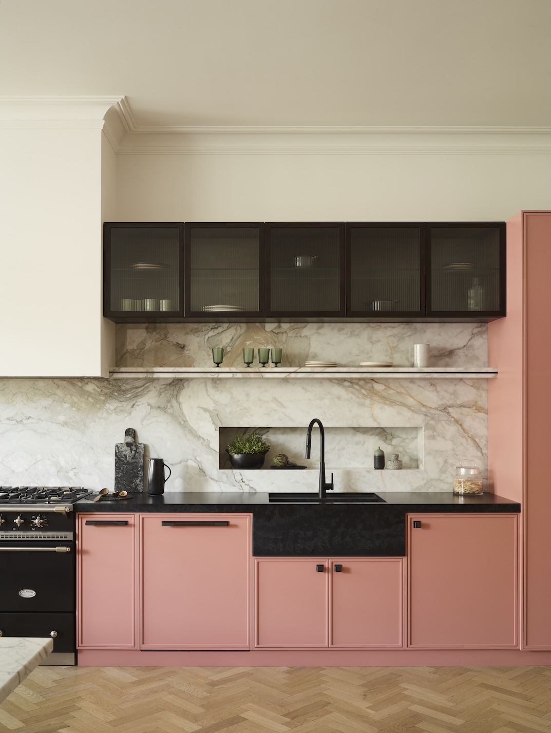 A salmon pink kitchen showing simple dark bronze handles and knobs with a black sink and black high level wall cabinets