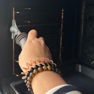 a woman's hand and arm with jewellery cleaning an oven rack with a steam cleaner