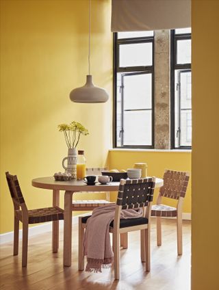 yellow dining room with round wooden table by Crown