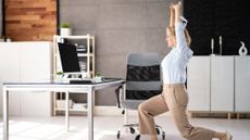 Woman in business attire stretches in front of a desk