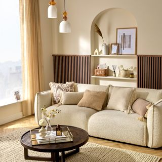 A living room with a cream boucle sofa adorned with mismatched cushions and an arched display behind it