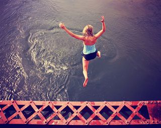 A woman leaps off a structure into water.