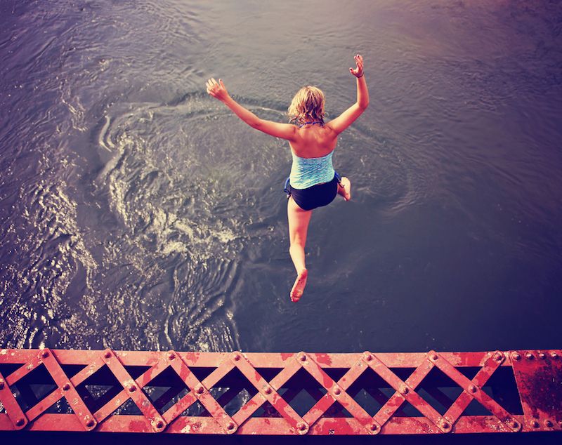 A woman leaps off a structure into water.