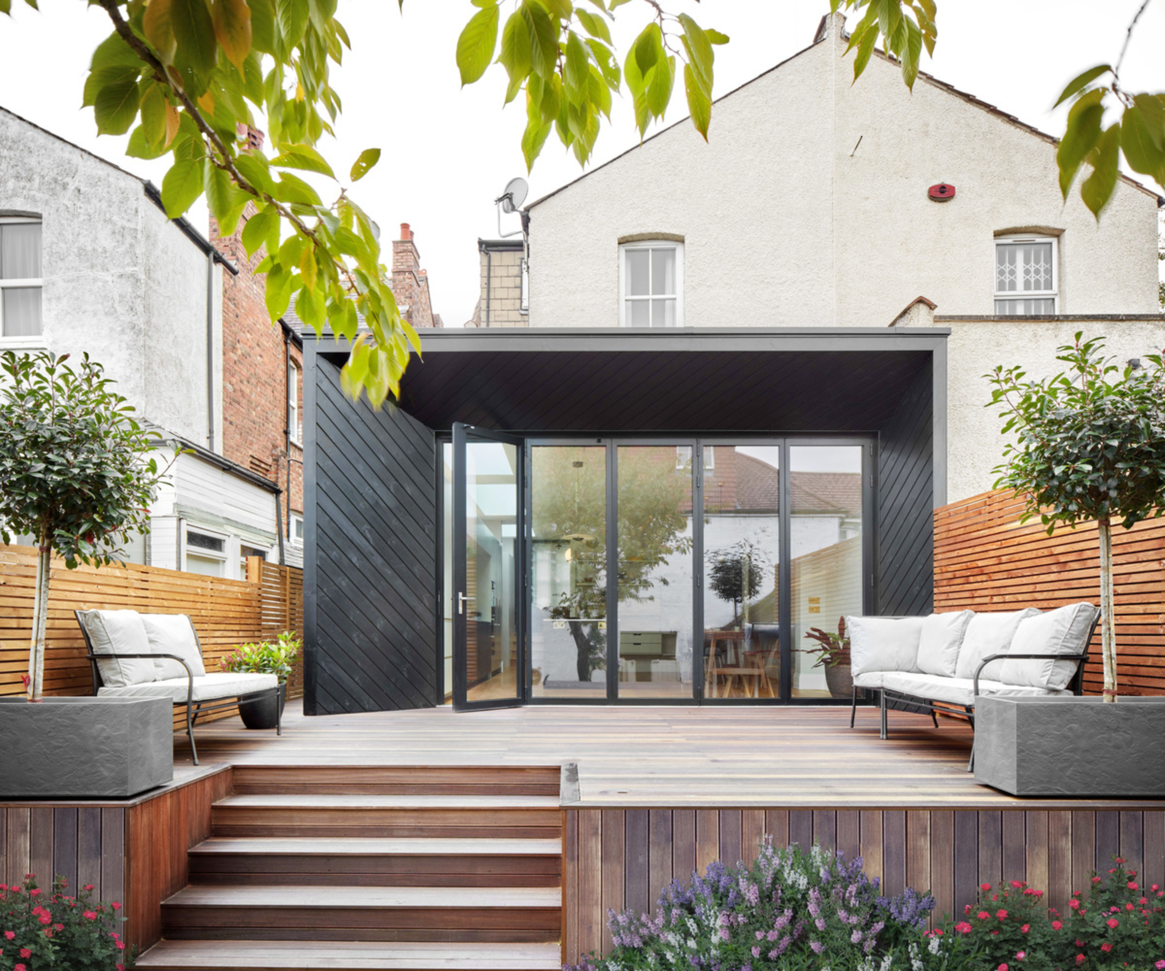 modern black clad wrap around extension on cream detached property, with decking area outside and built in steps leading down to garden