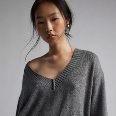 Urban Outiftters model wears v-neck grey knit sweater with silver earrings.