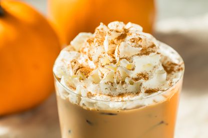 pumpkin spice latte in a glass next to real pumpkins