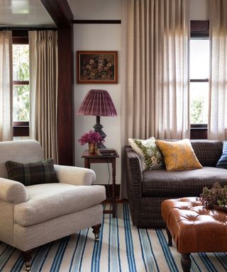Cozy living room with blue striped rug, cozy sofa and armchair, leather ottoman, sheer curtains