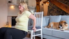 Woman exercising using a chair in front of a couch with a dog on it