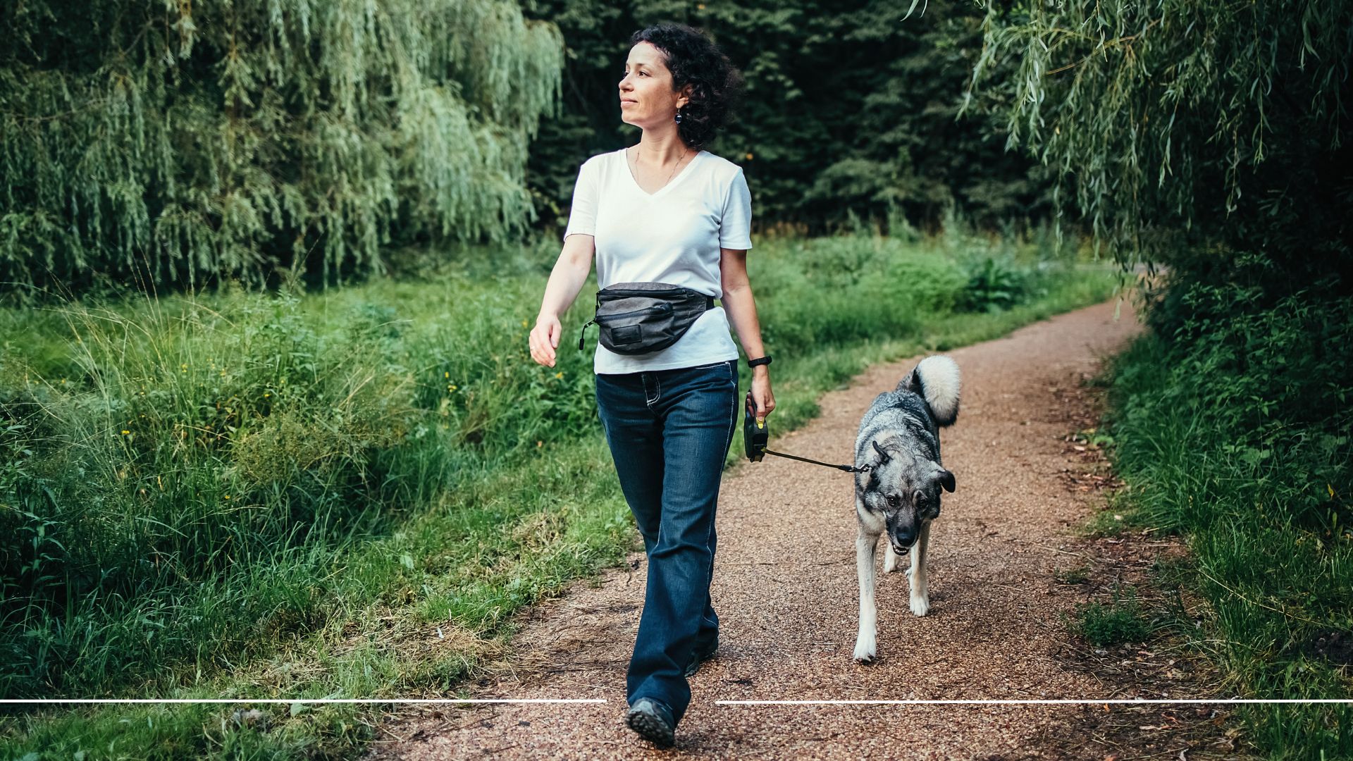 Woman walking in jeans and top over canal path with bum bag and dog, representing the benefits of walking outdoors
