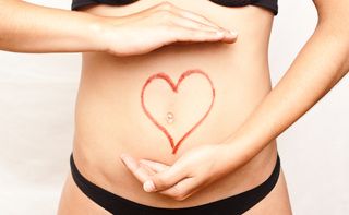 A woman stands with a heart drawn onto her belly.