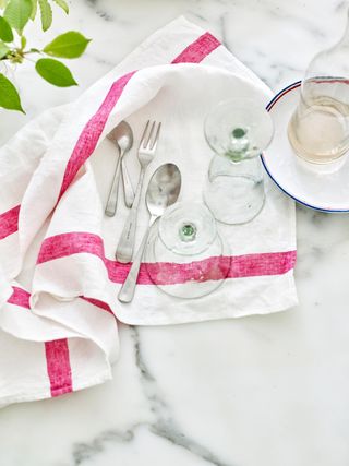 Flatware and two glasses drying on a white towel with pink strips on top of a marble countertop.