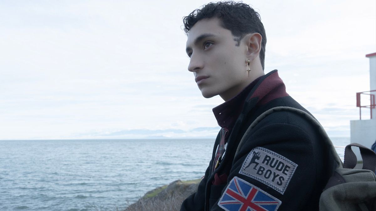 A boy looks out over the ocean wearing a jacket with a &#039;rude boy&#039; and union jack patches