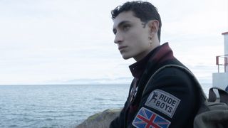 A boy looks out over the ocean wearing a jacket with a &#039;rude boy&#039; and union jack patches