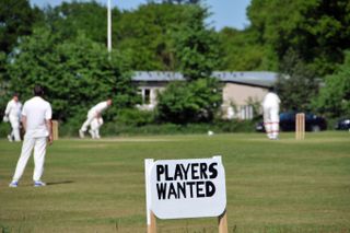 Village green cricket match and sign for players wanted