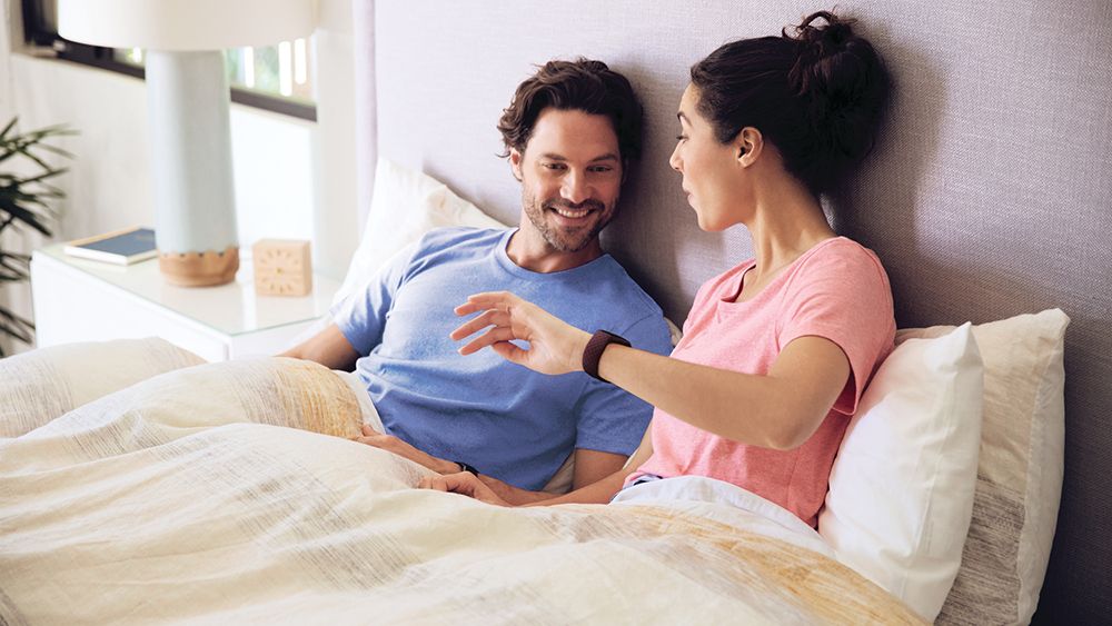 Couple in bed looking at sleep tracker on woman&#039;s wrist