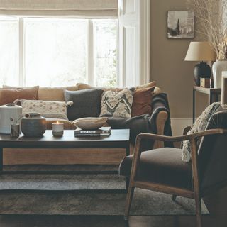 A neutral-coloured living room with a light brown sofa with contrasting cushions and throws and a dark brown accent chair