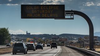 cars lined up on a highway under a sign reading "solar eclipse saturday major delays"