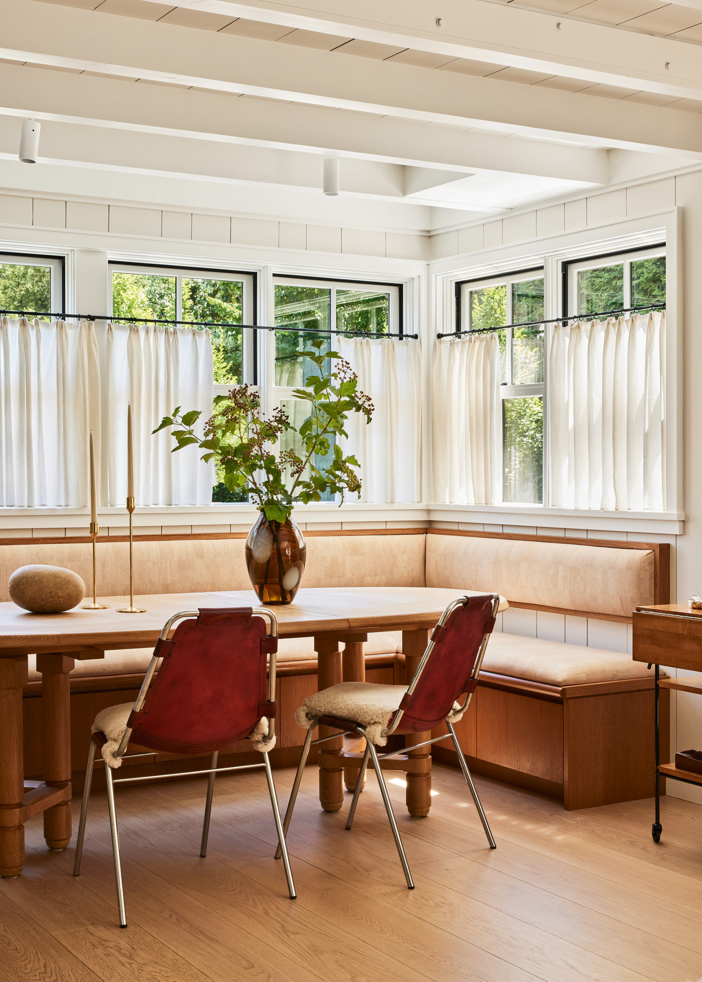 Dining area with wood and cream upholstery corner banquette seating, wood dining table and burgundy leather and chrome dining chairs