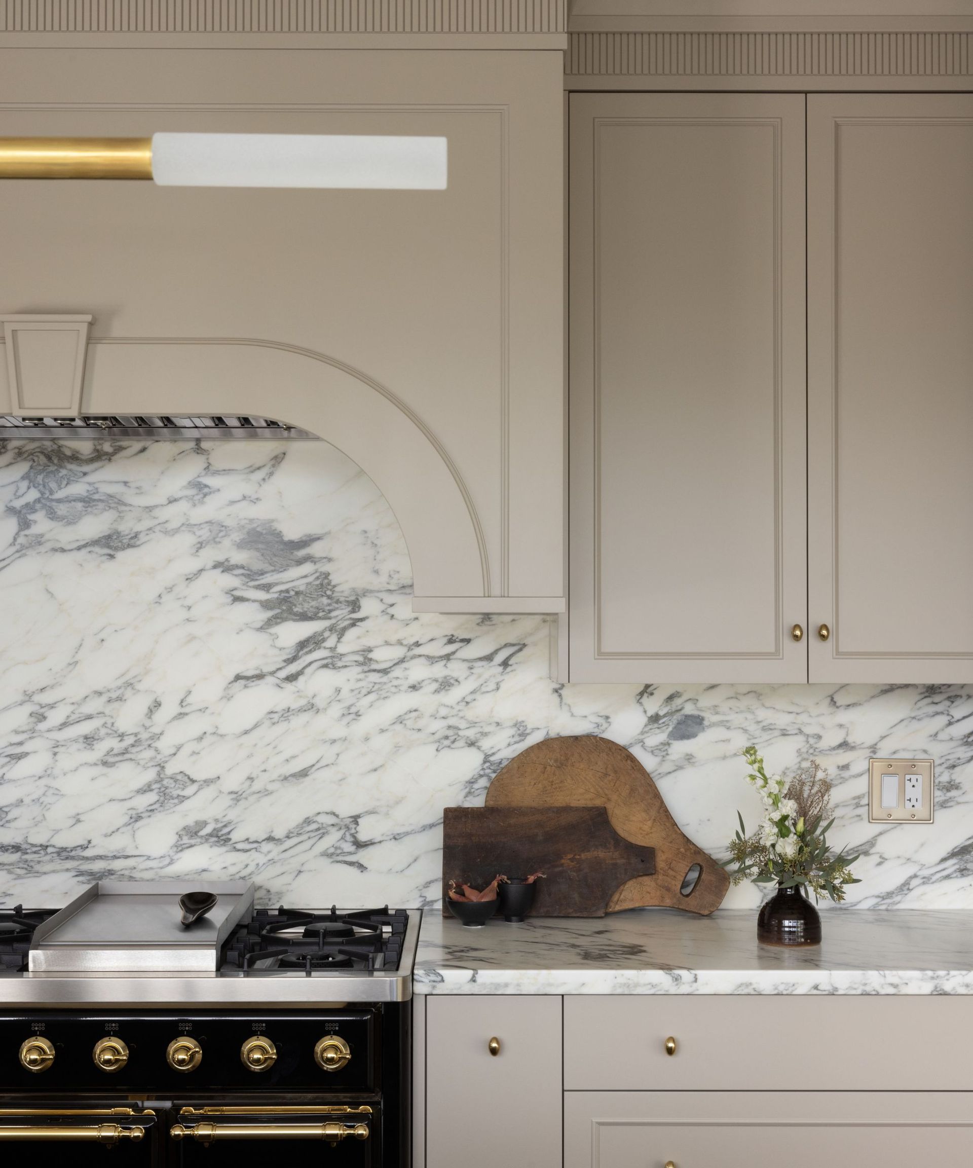 beige kitchen cabinets with marble backsplash and arched detail over range cooker