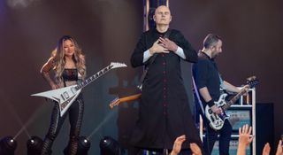 Billy Corgan closes his eyes and places his hands on his chest as he is flanked by new Smashing Pumpkins guitarist Kiki Wong with her Rhoads V, and touring bassist Jack Bates.