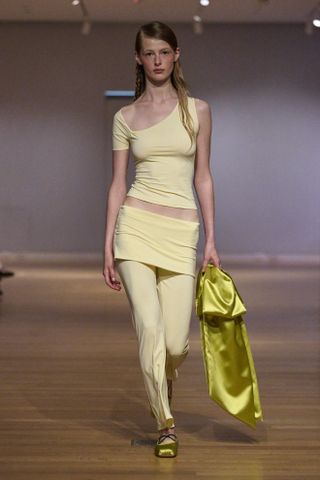 Sandy Liang model wearing a yellow knit top and skirt-over-pants look with green satin accessories at the spring/summer 2024 show.
