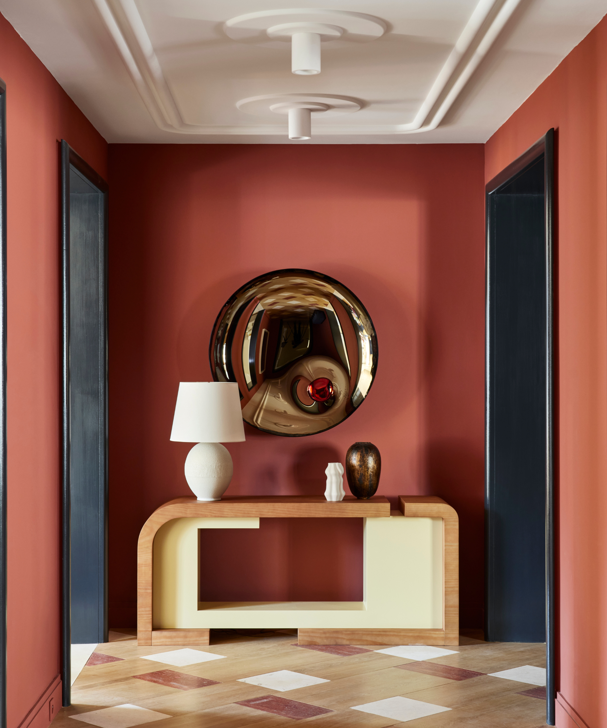 Warm red tone walls and tile floor in hallway with round mirror and black door frames to punctuate the space