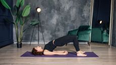 Woman doing glute bridge on two legs, one of the best exercises for women over 50 at home on yoga mat in studio