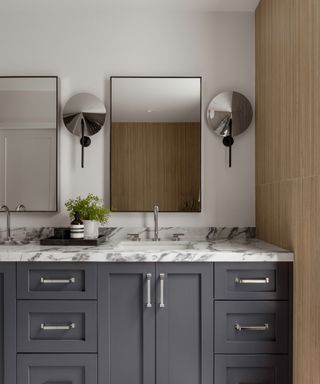 bathroom with dark gray cabinets, silver hardware, marble countertops, double sink with rectangle mirrors above and off-white walls