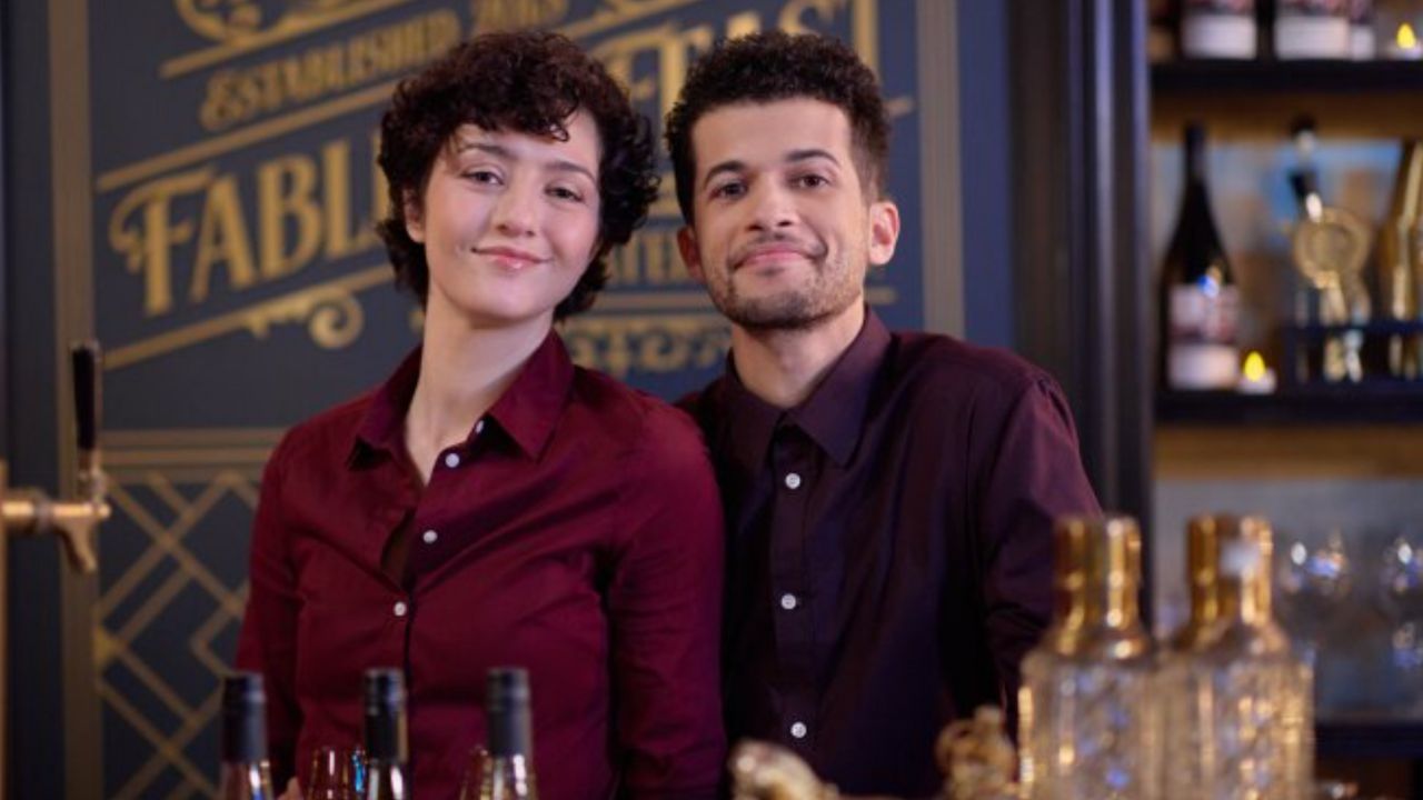 Alice and Max smiling directly at the camera behind the mar in The 5-Year Christmas Party