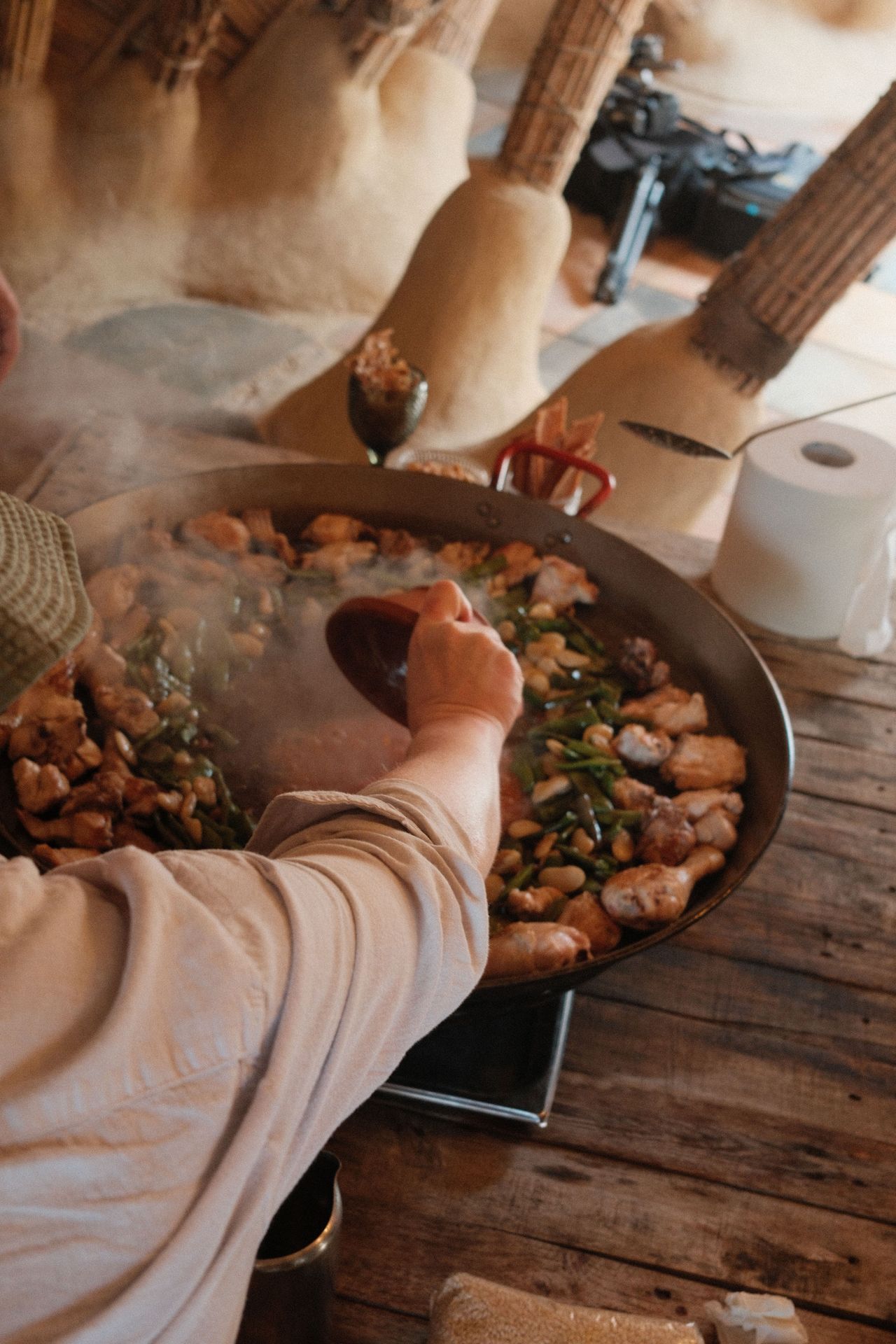 A hand reaching over to pout more ingredients into a paella pan