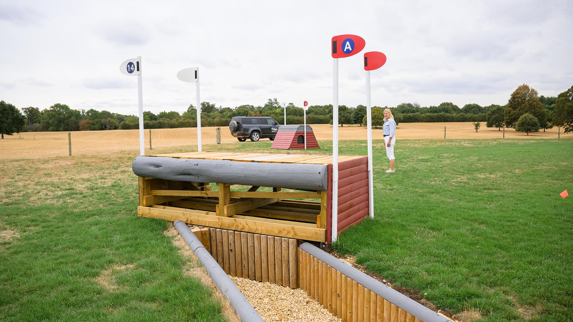A spread fence angled with a ditch in front of it, on the Burghley cross-country course 2026, with event rider Tina Cook in the background