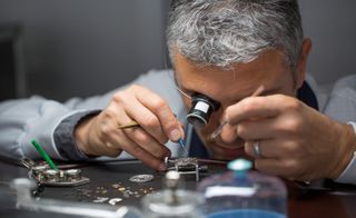 A watch maker wearing a magnifying glass on one eye and holding tools.