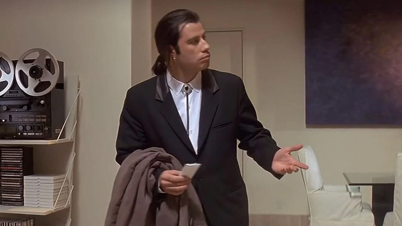 John Travolta holding is hand out, looking confused.
