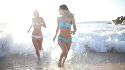 Two women in bikinis running out of the sea towards the beach