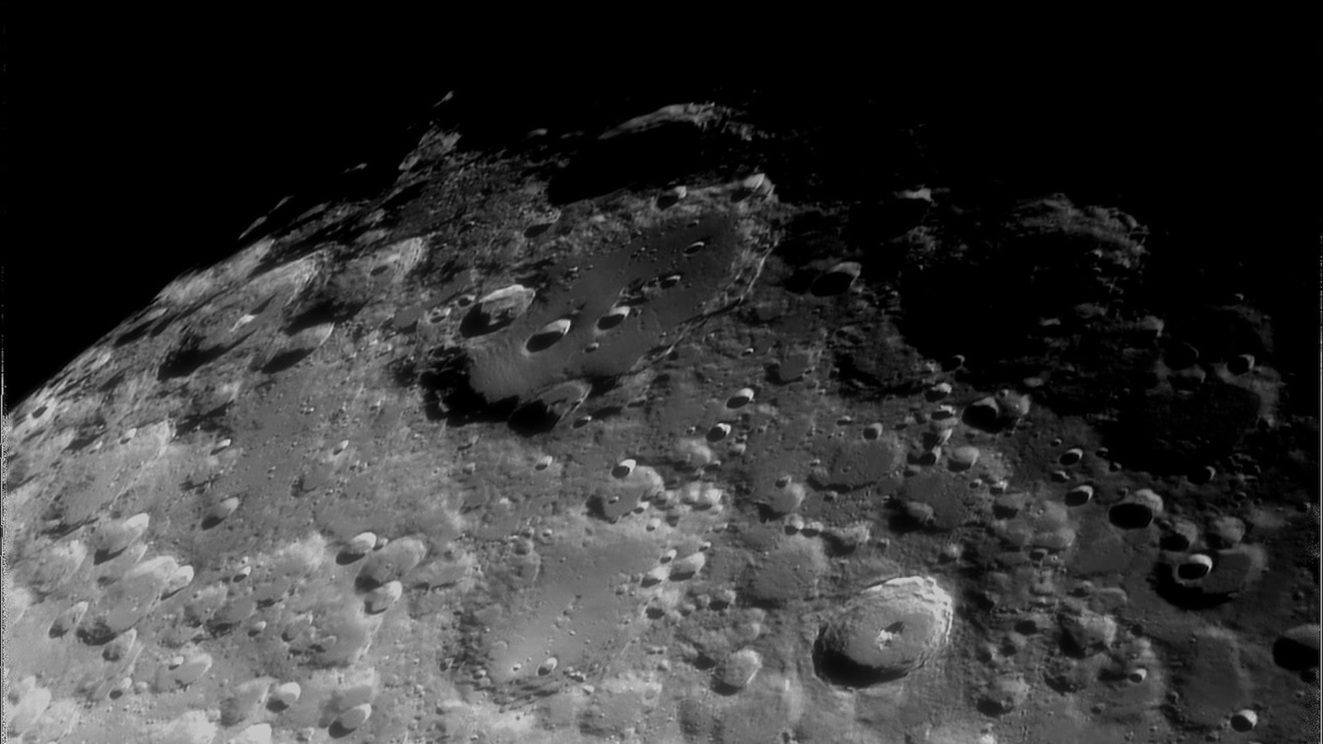 A close up look at the surface of the moon, with its many gray dusty craters, with some in shadow and darkness from space