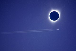 an aircraft flies through the sky directly beside the moon as it blocks out the sun in the sky