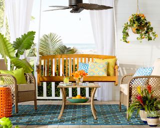 Colorful front porch ideas by Wayfair with orange side table, wooden bench and rattan seats