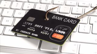 A bank card skewered on the end of a fishhook in front of a white computer keyboard.