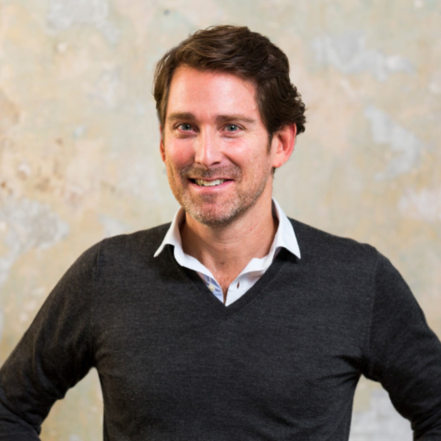 A headshot of a man in a black sweater and a white shirt