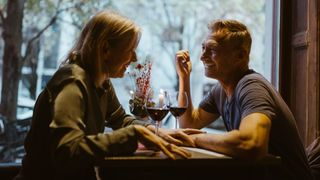 Woman and man sitting at table in the window of a pub with glasses of red wine, laughing and smiling, building intimacy in a relationship