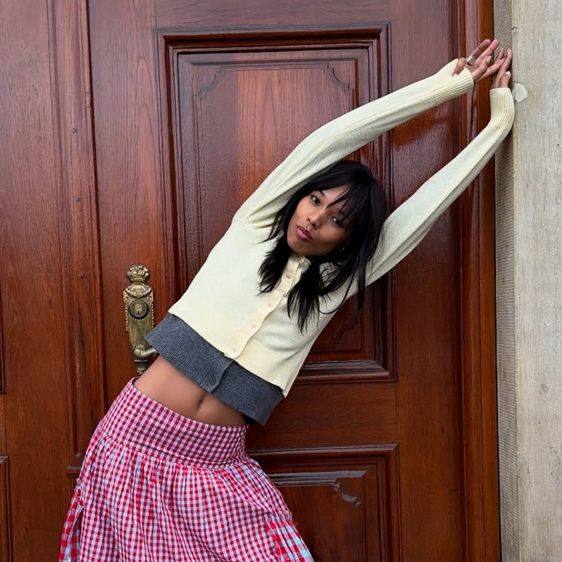 a woman wearing a yellow cardigan and red gingham skirt