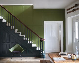A hallway and staircase in two tones of green, with stone flooring and one white wall.