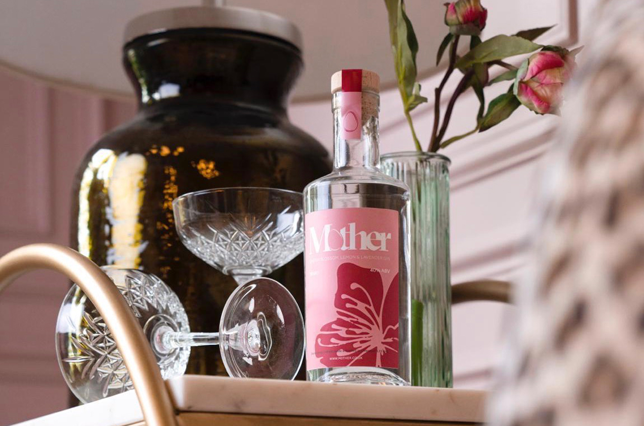 Bottle of gin on a drinks trolley with glasses and a vase of roses