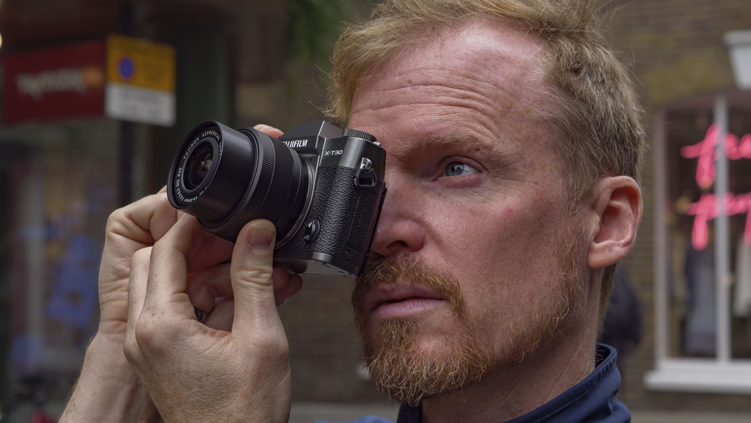 Man holding the Fujifilm X-T30 III camera up to his eye, on London street