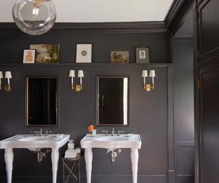 bathroom with dark gray walls, white double sinks and mirrors