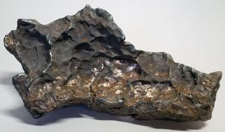 a dark, shiny iron meteorite rests on a white surface